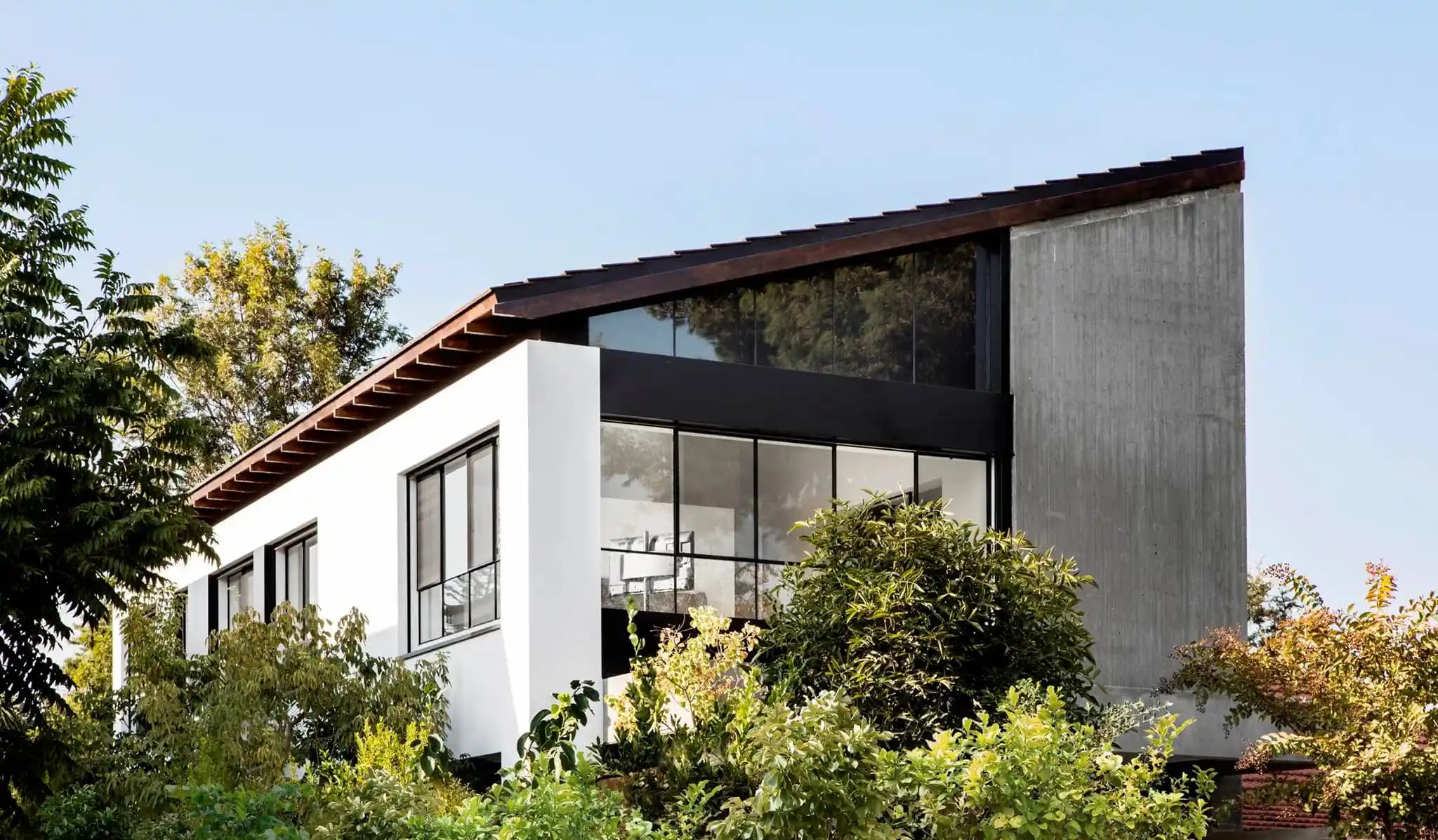 בית מודרני דו קומתי עם גג רעפים וחלונות גדולים מוקפים בצמחייה