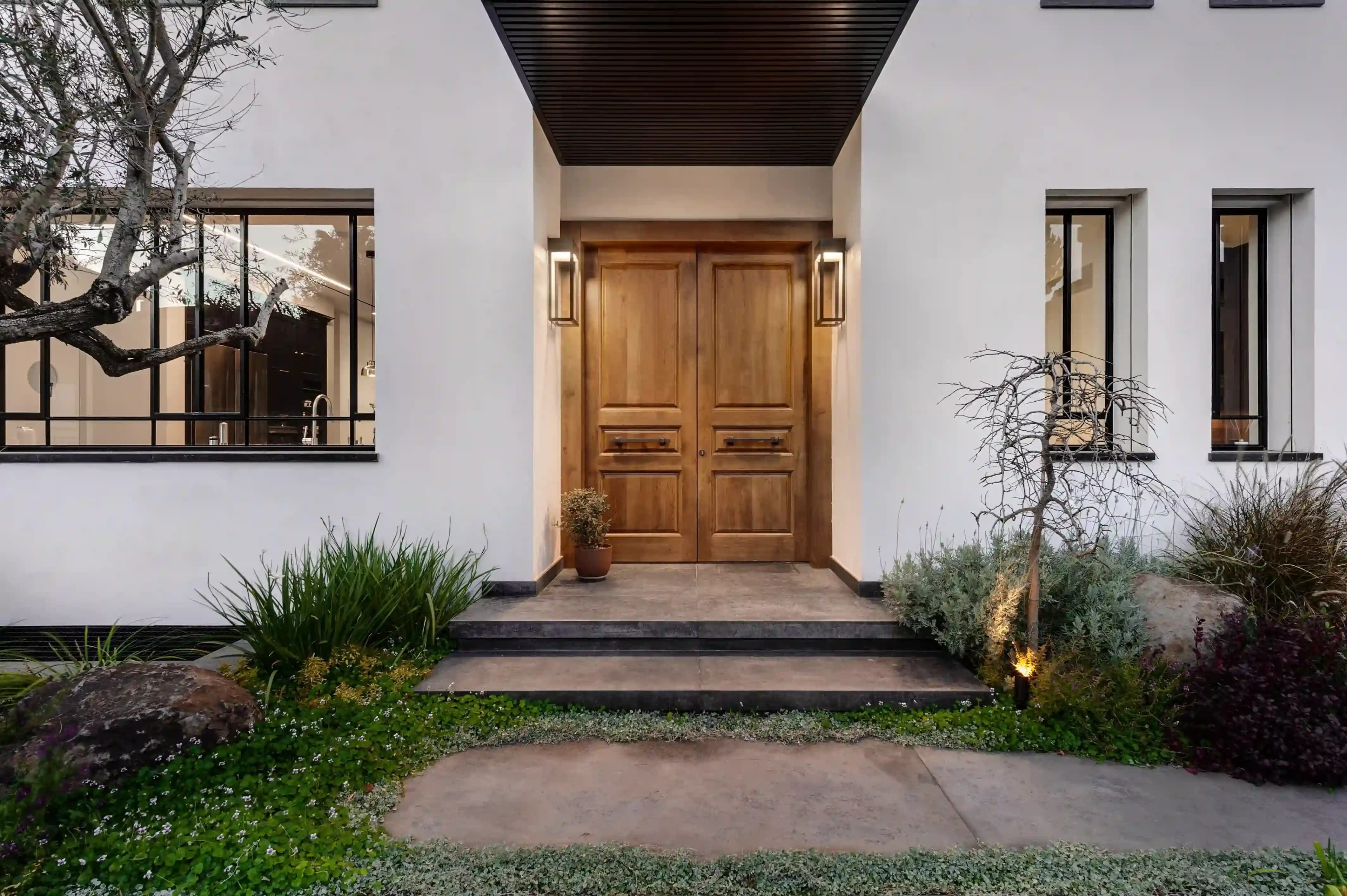 כניסה מעוצבת לבית פרטי עם דלת עץ מפוארת ותאורה אדריכלית