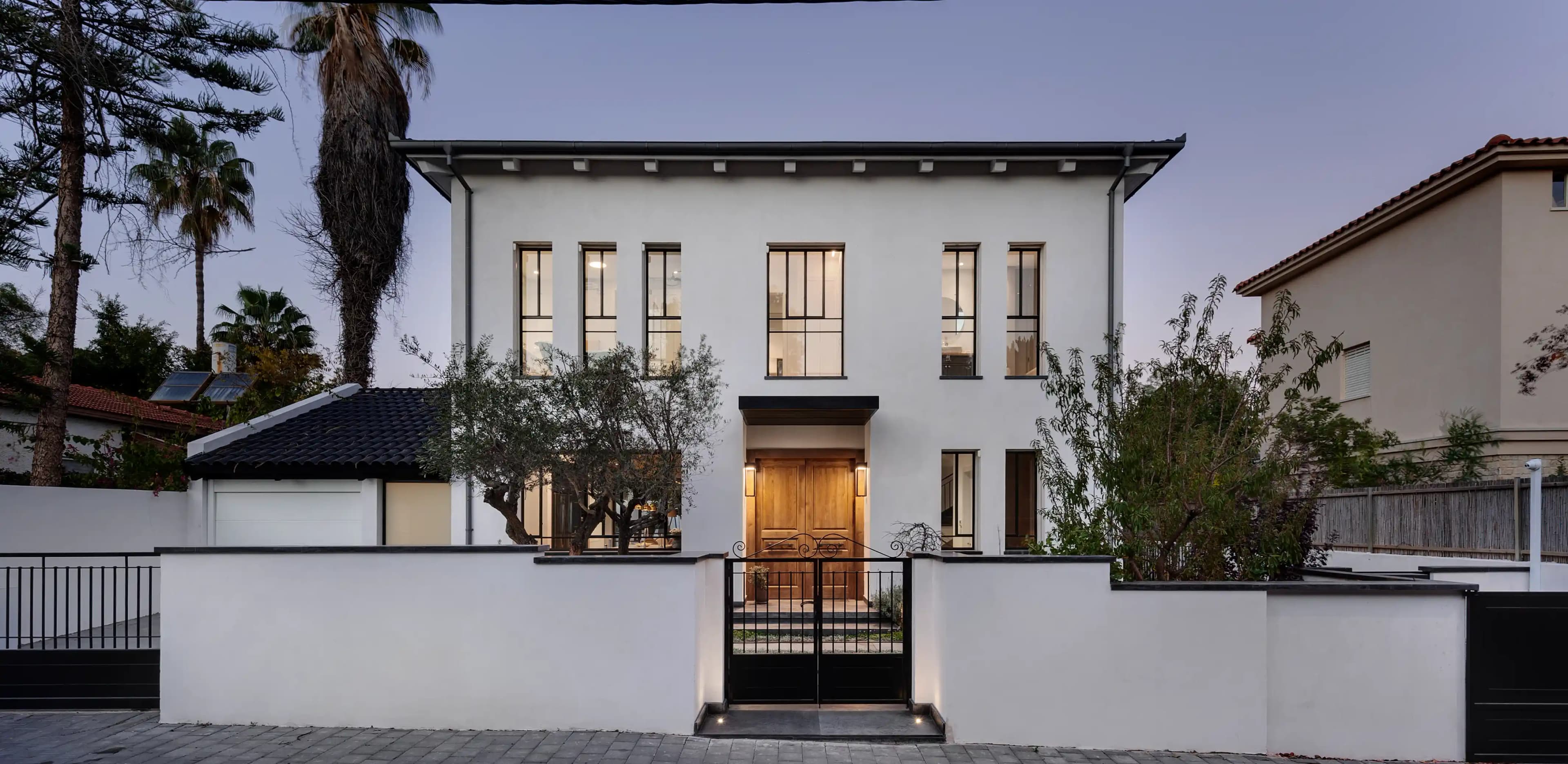 חזית בית פרטי לבן עם חלונות גדולים ושער ברזל מעוצב