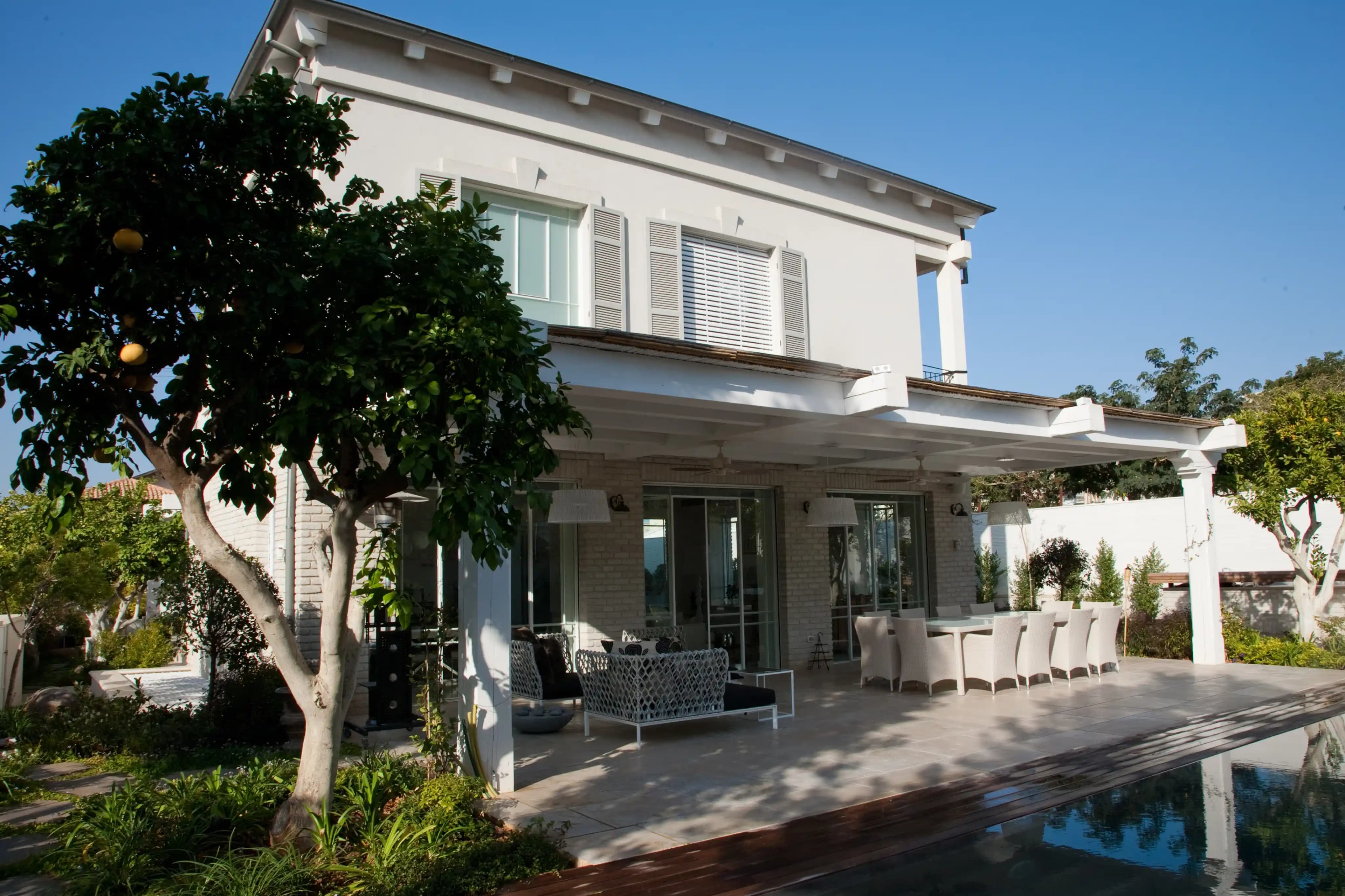 בית פרטי לבן עם פרגולה ומרפסת מוצלת ליד בריכת שחייה